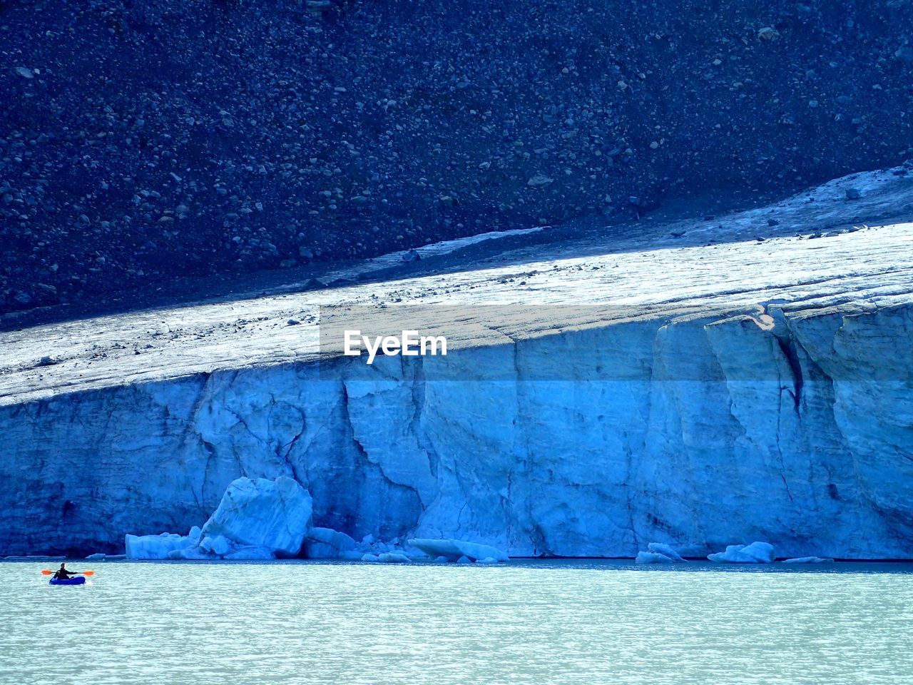 Person kayaking on sea by iceberg