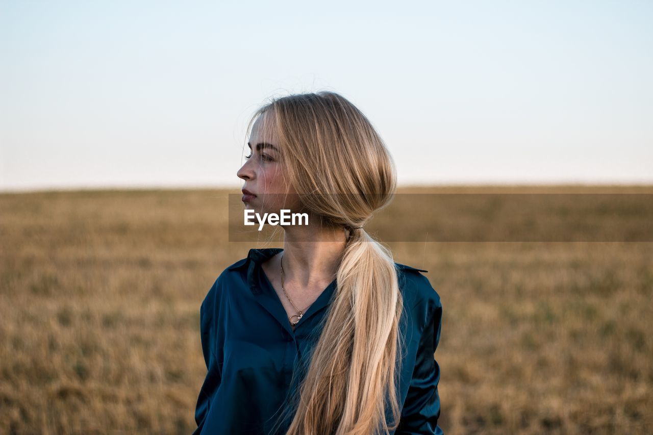 Thoughtful young woman standing on field against clear sky