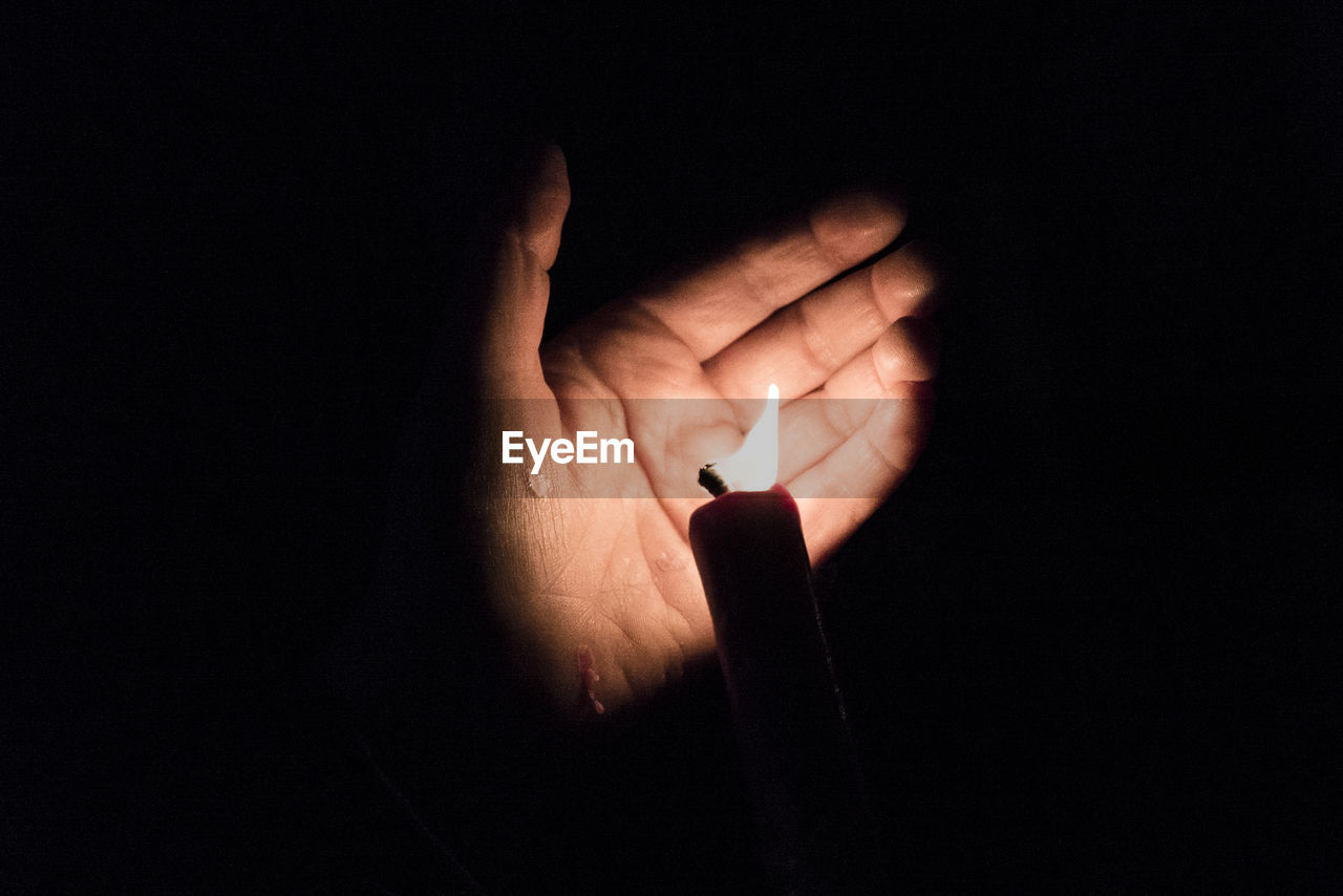 Cropped hand with lit candle in darkroom