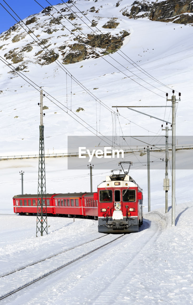 TRAIN ON SNOW COVERED RAILROAD TRACKS BY MOUNTAIN