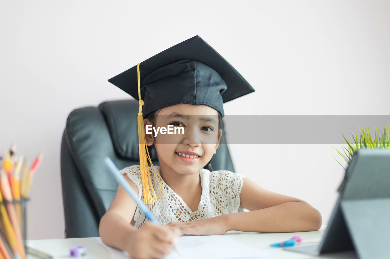 Portrait of smiling girl holding pen over paper on table