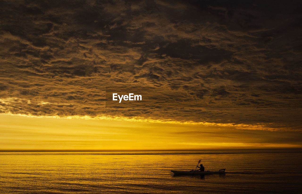 Silhouette man sailing in boat on sea against cloudy sky during sunset