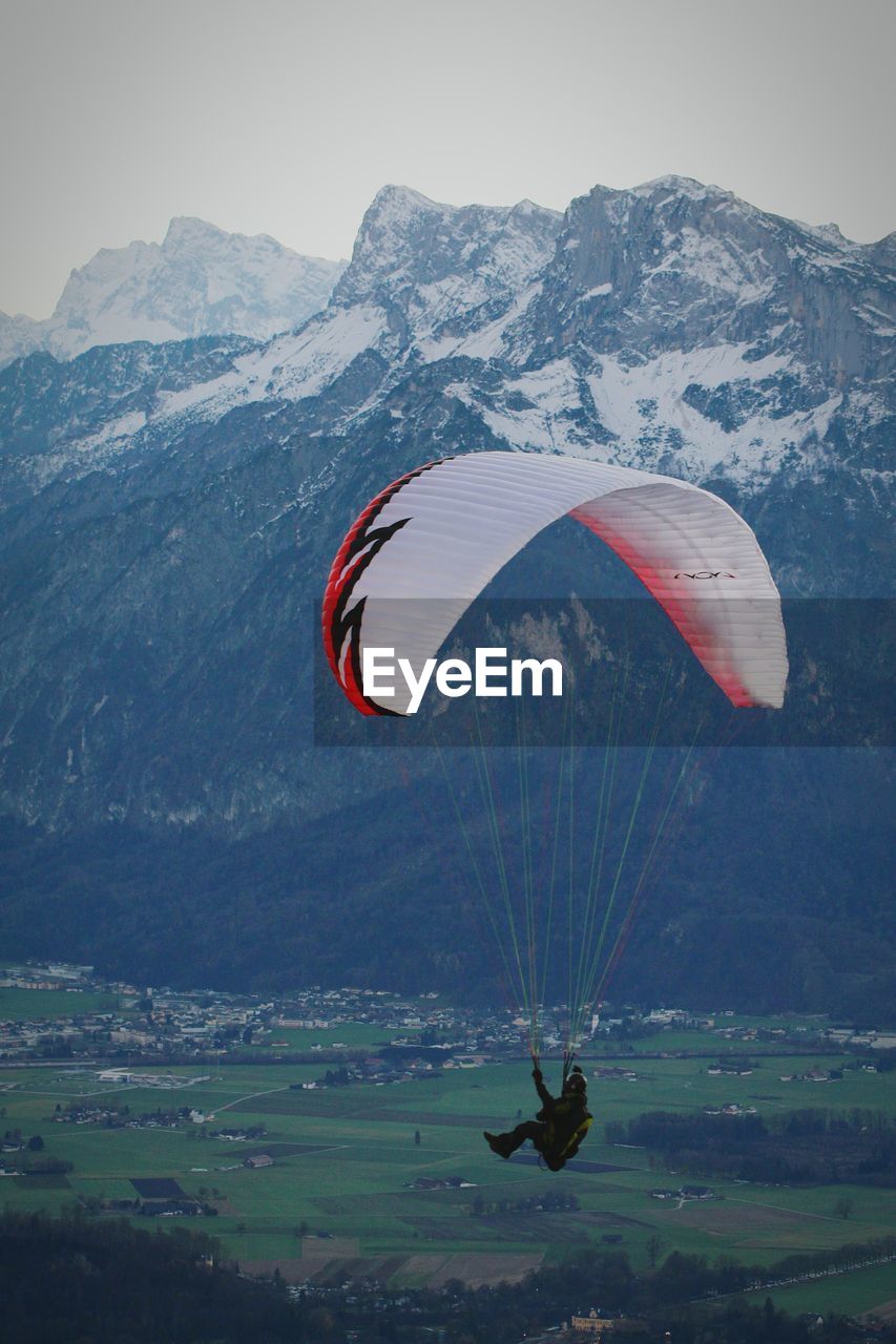 Person paragliding over field against mountains