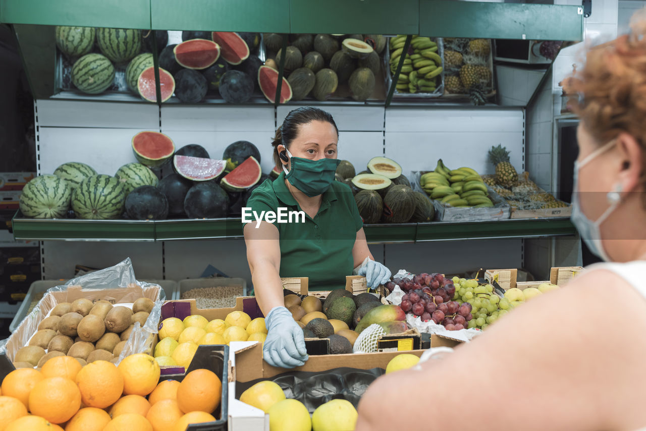 A shopkeeper with a mask attends to a customer in the greengrocer's.