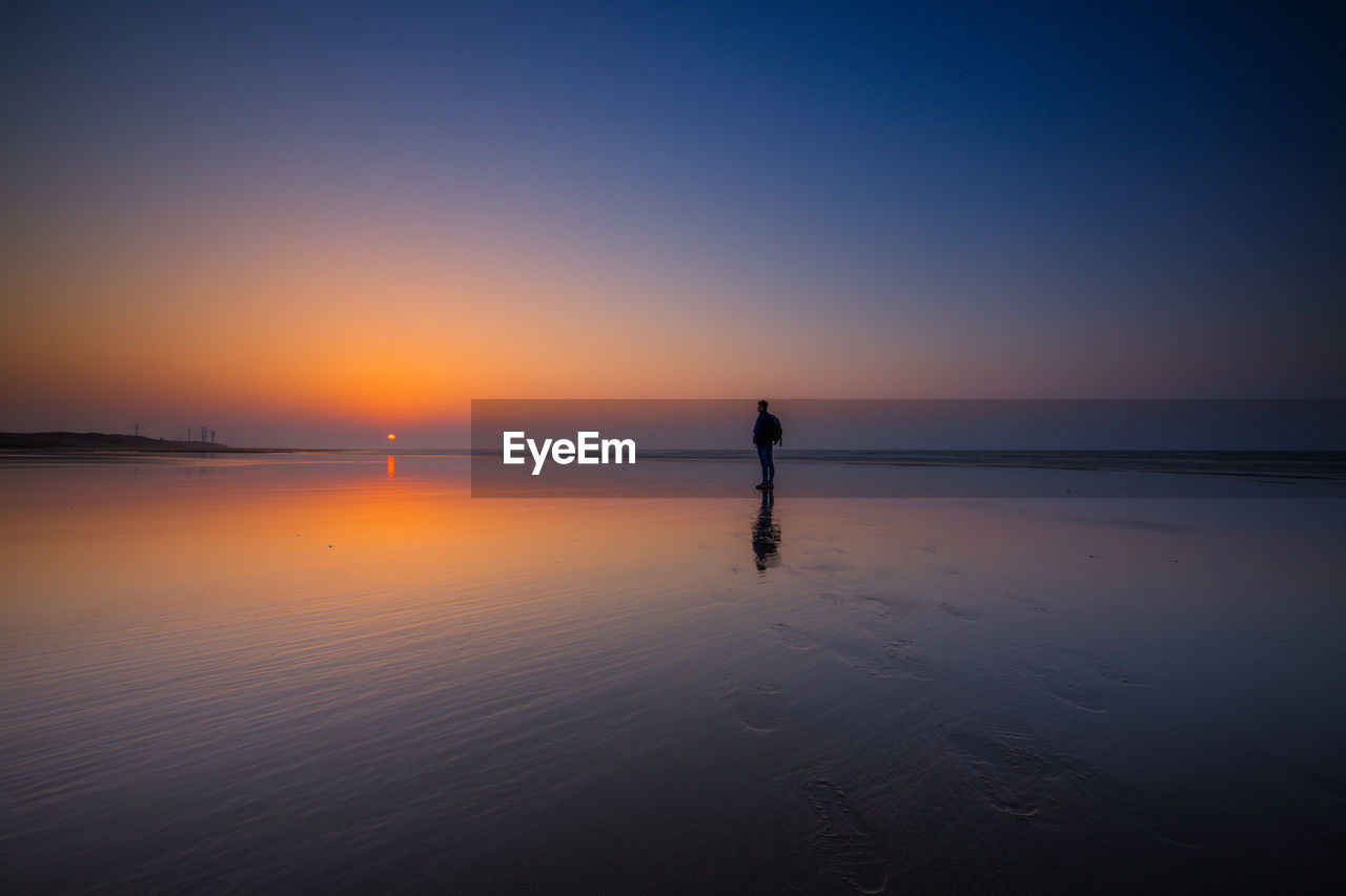 Silhouette man standing on beach against sky during sunset