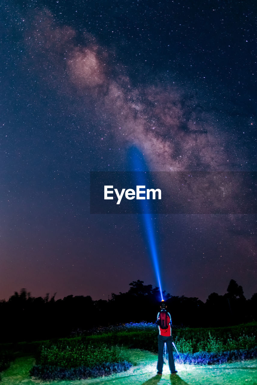 Rear view of man with flashlight standing against star field