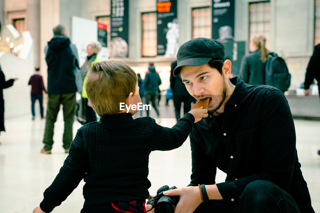 Son feeding food to father in city