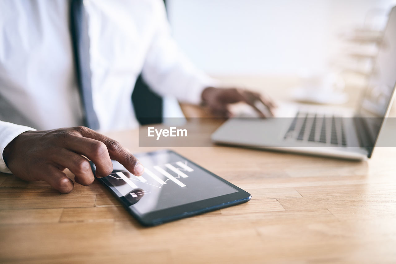 midsection of man using mobile phone on table in office