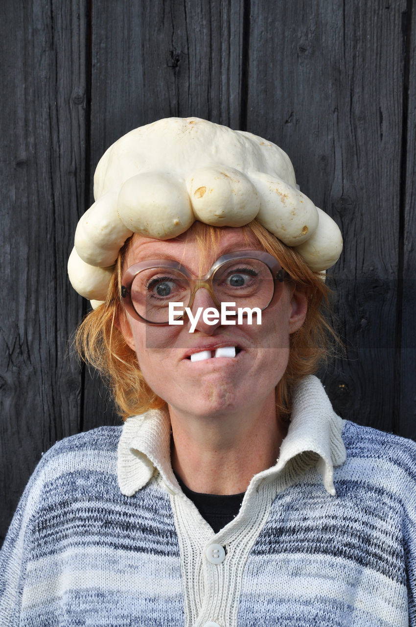 Mature woman wearing artificial pumpkin hat and making face