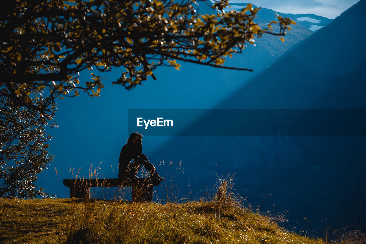 Woman sitting bench at field against mountain