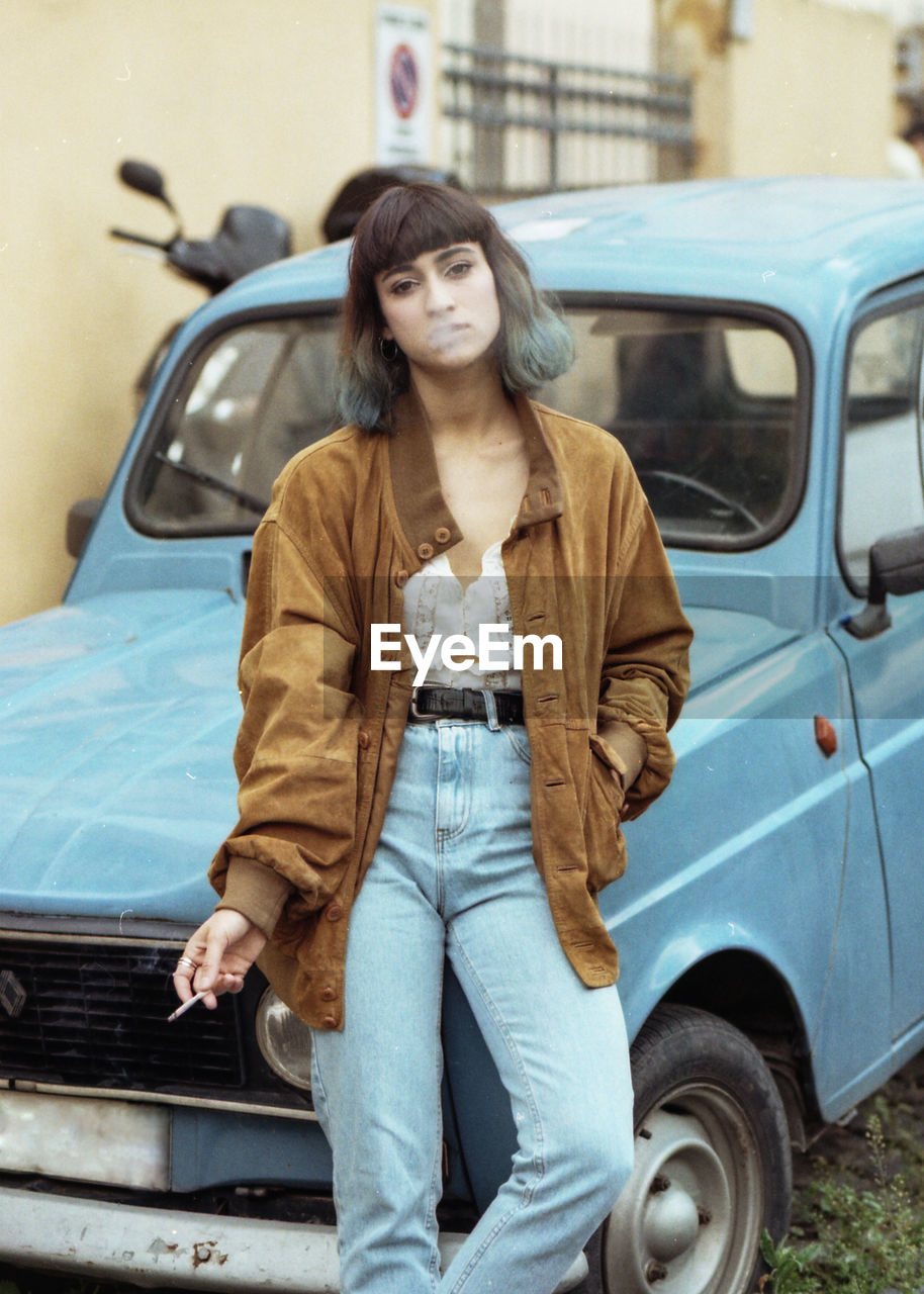 Portrait of woman smoking cigarette while leaning on car