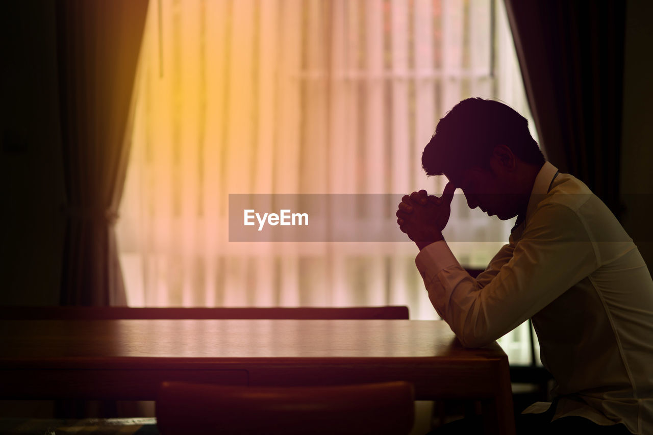 SIDE VIEW OF MAN SITTING ON TABLE