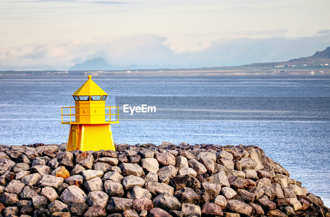 Yellow lighthouse by sea against cloudy sky