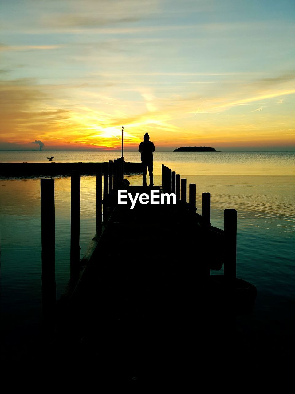 Silhouette of people standing on pier at sunset