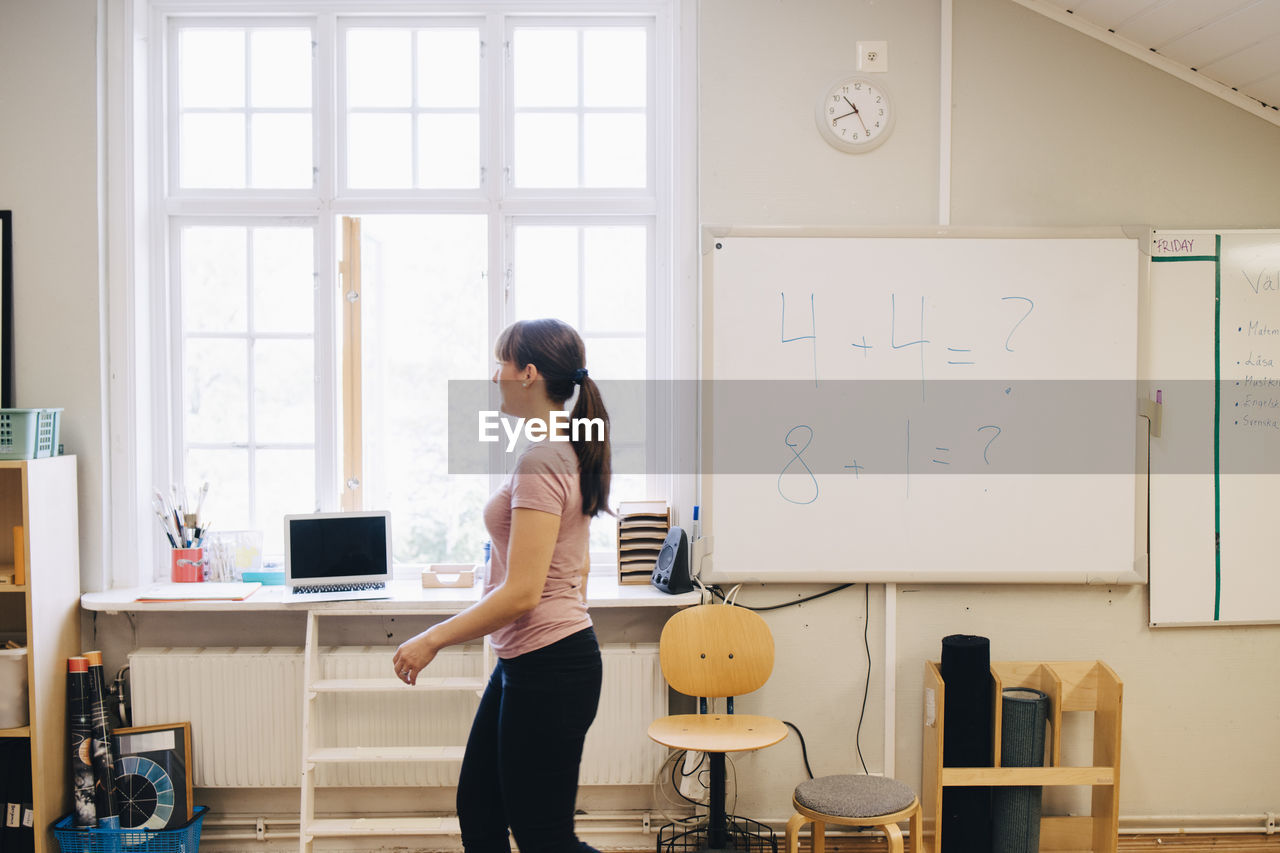 Side view of teacher walking by whiteboard with mathematics in classroom