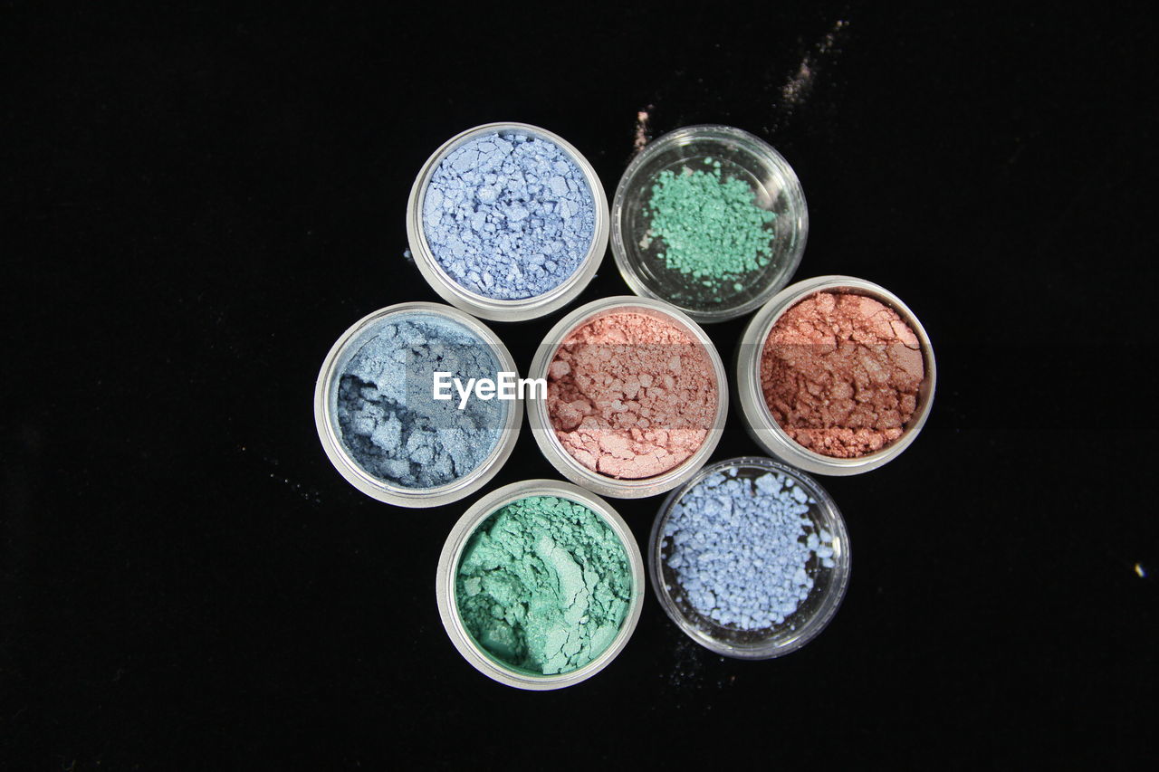 Directly above shot of multi colored face powder in containers against black background