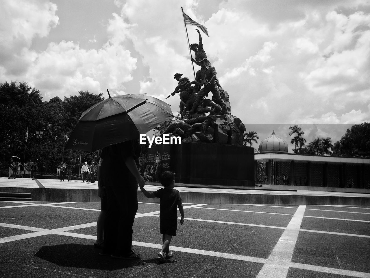 Rear view of woman with son under umbrella walking at war memorial 