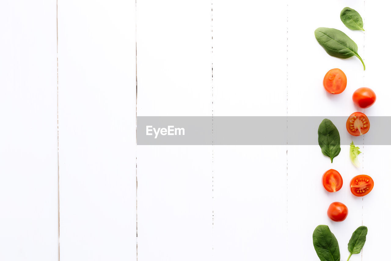 Flat lay with red cherry tomatoes and green spinach leaves on a white wooden background