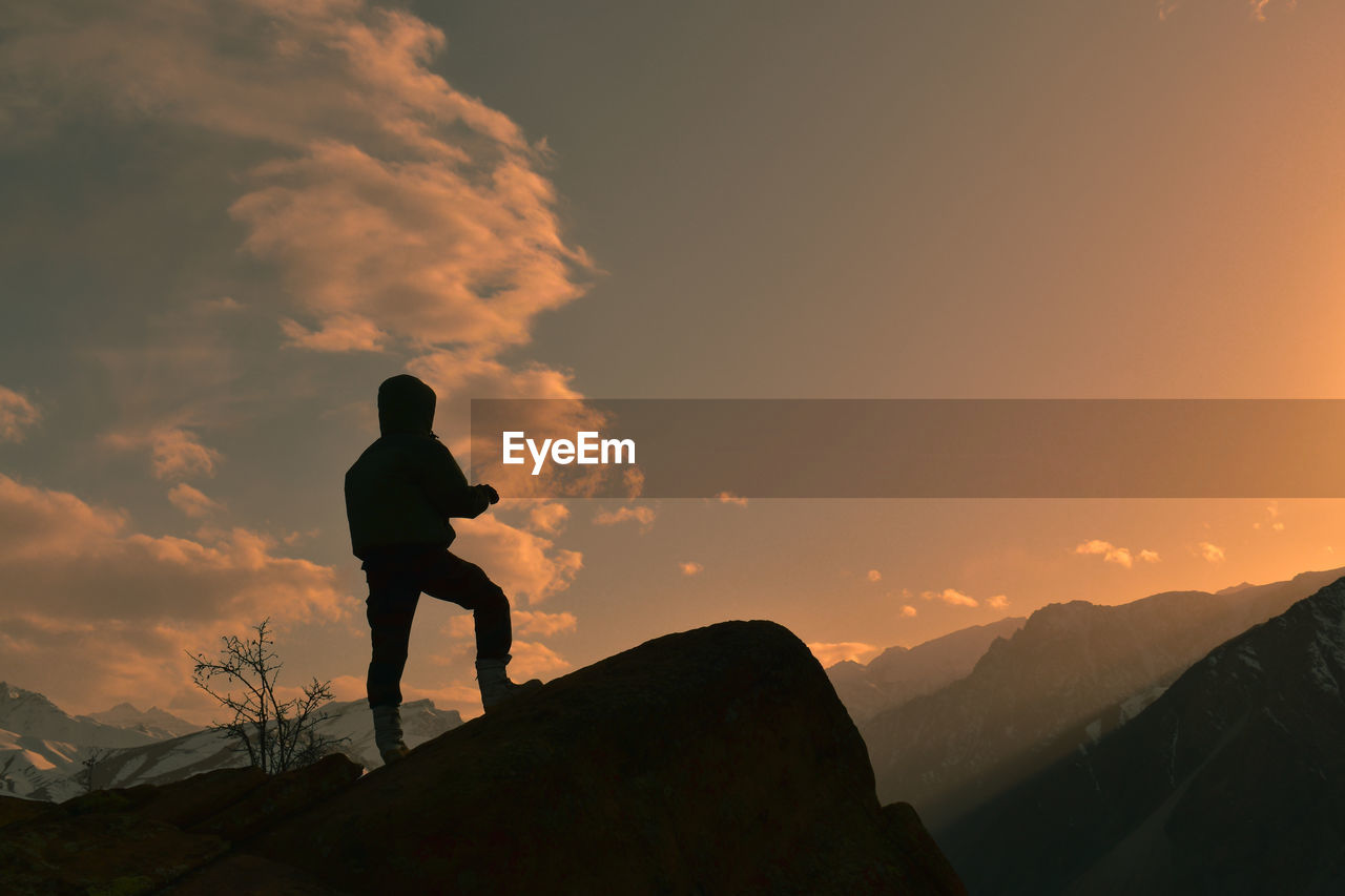 Rear view of man standing on mountain against sky during sunset