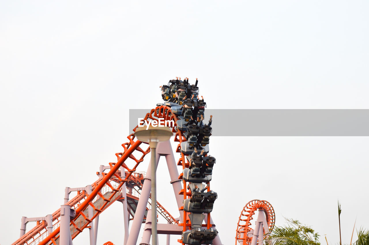 Low angle view of people enjoying rollercoaster ride at amusement park against clear sky