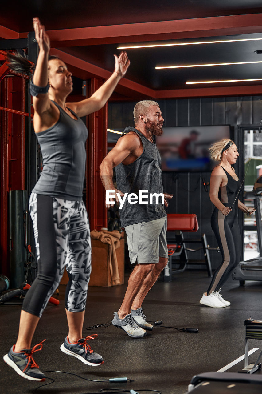 full length of young woman with arms raised standing in gym