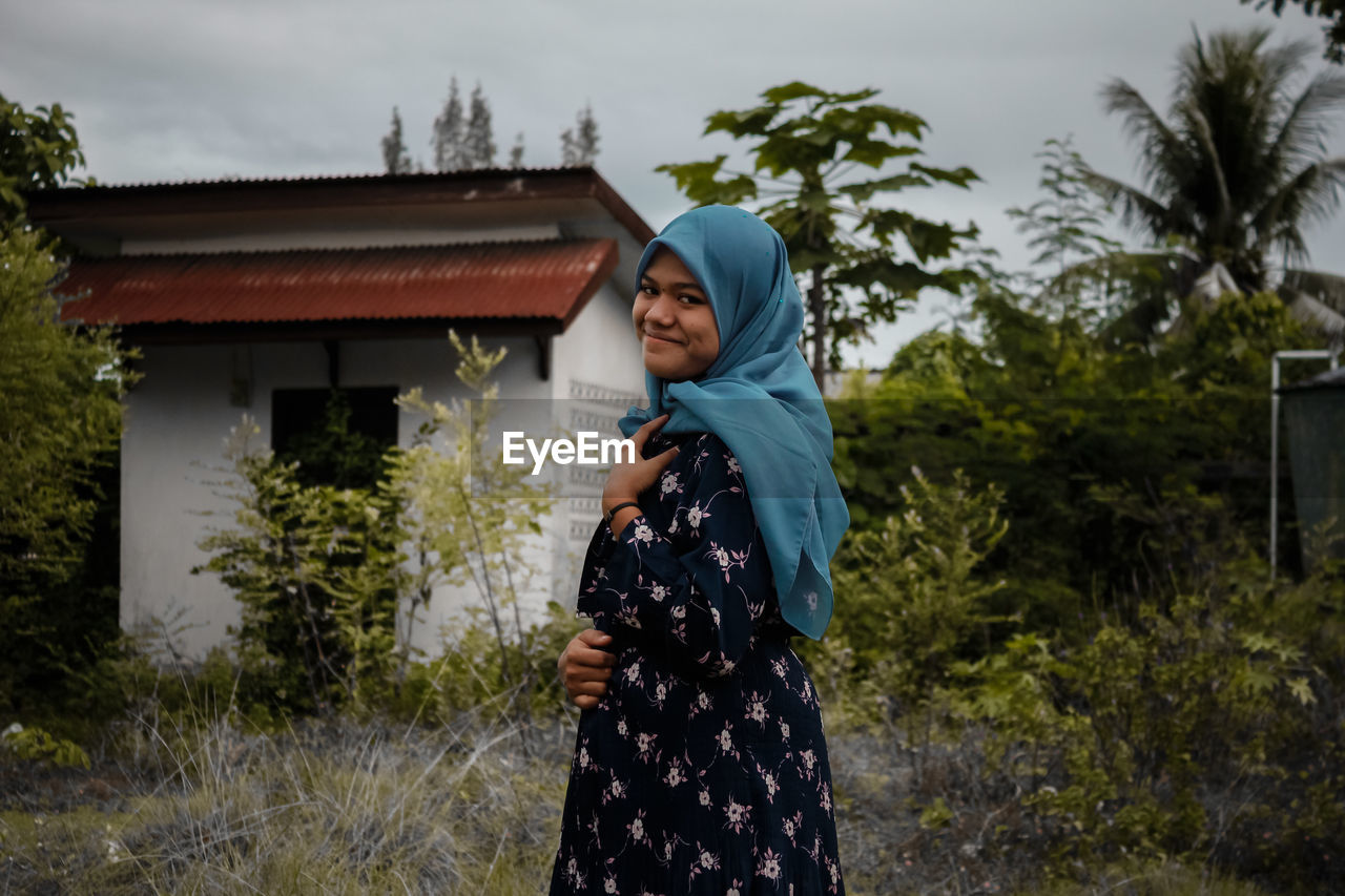 Woman standing by building against trees and house