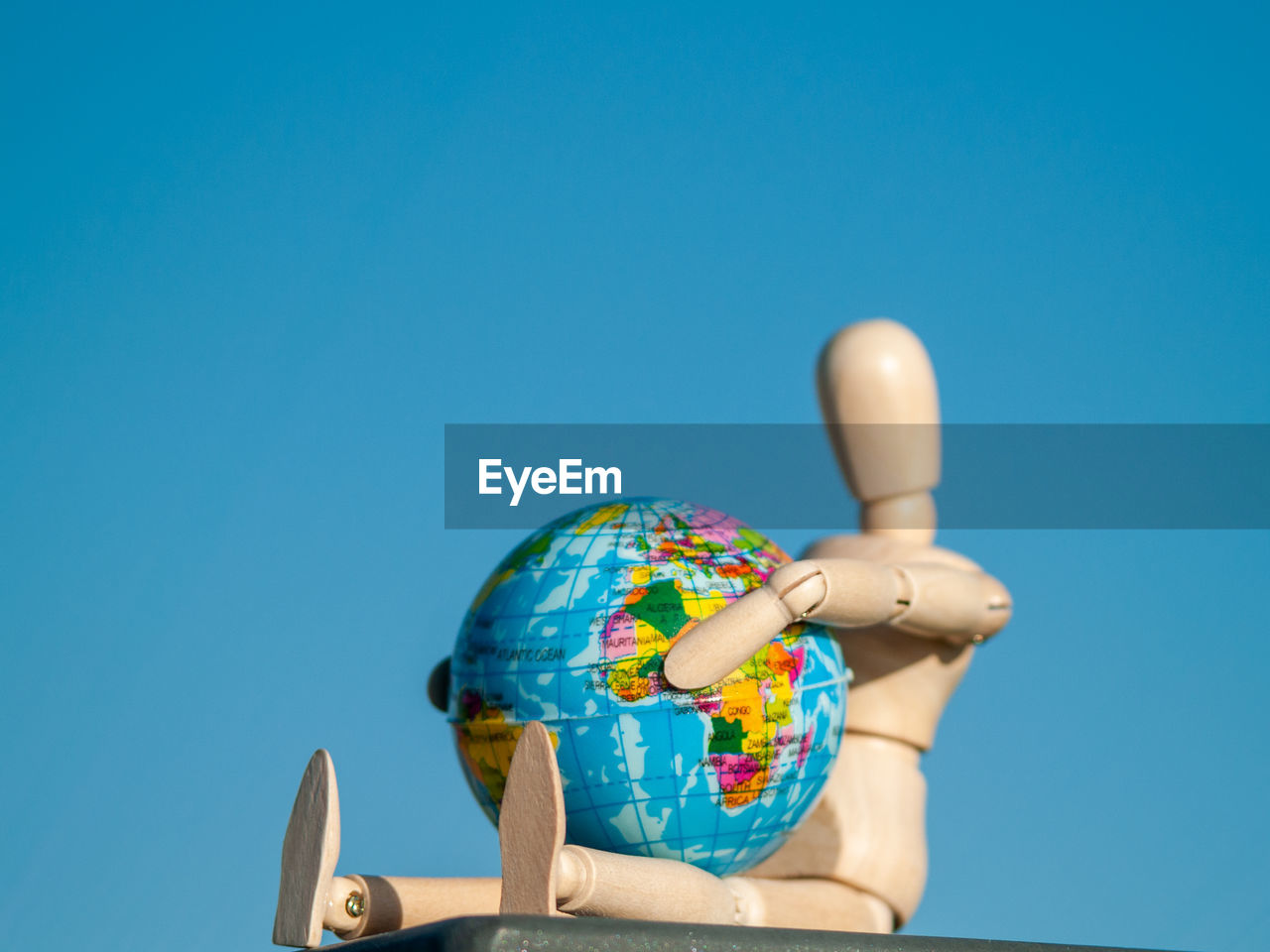 Close-up of globe and wooden figurine against clear blue sky