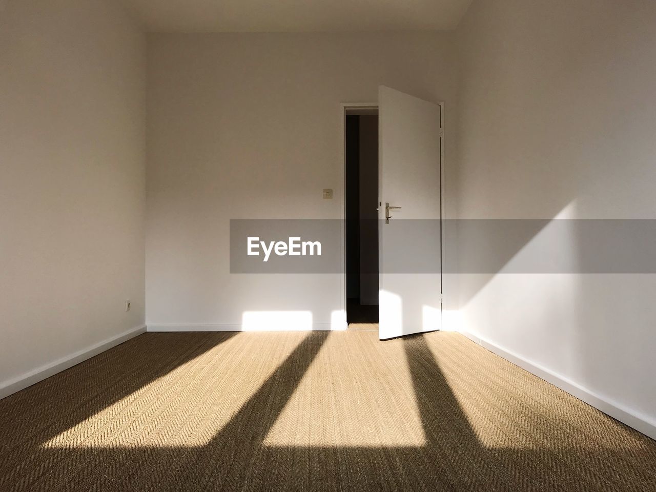 Sunlight falling on empty apartment room, white painted walls and brown carpet