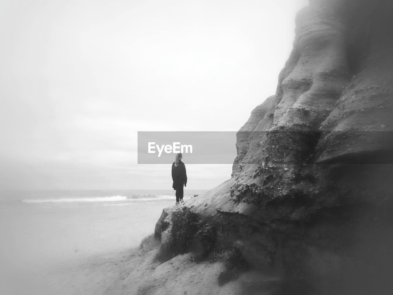 Rear view of girl standing on rock formation at beach against sky