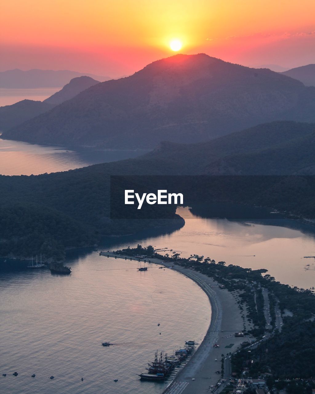 HIGH ANGLE VIEW OF MOUNTAINS BY SEA AGAINST SKY DURING SUNSET