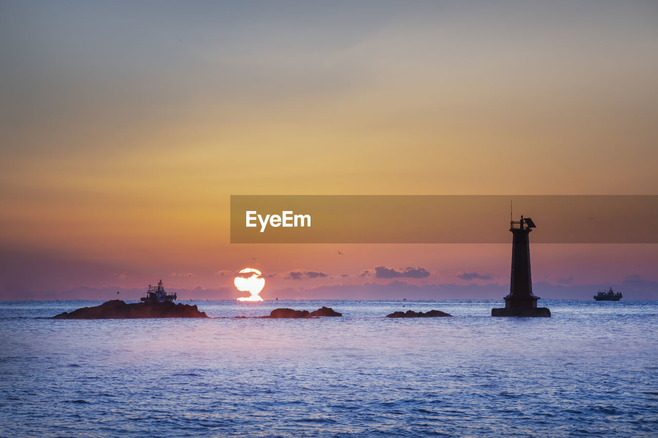 LIGHTHOUSE BY SEA AGAINST ORANGE SKY