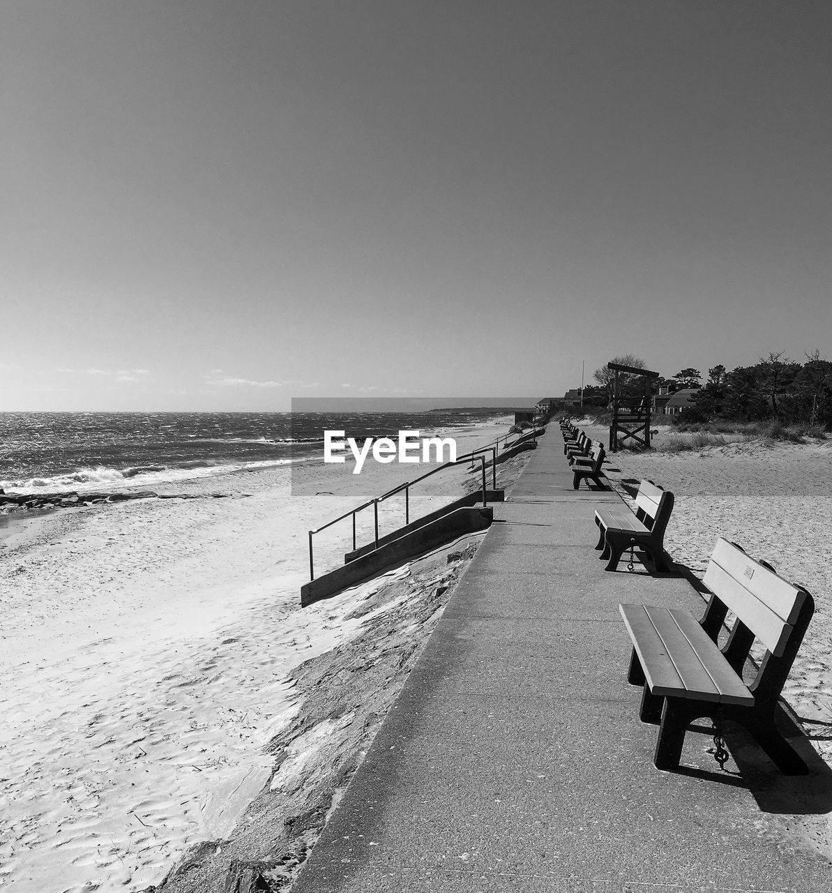 Empty benches on beach against clear sky in black and white 