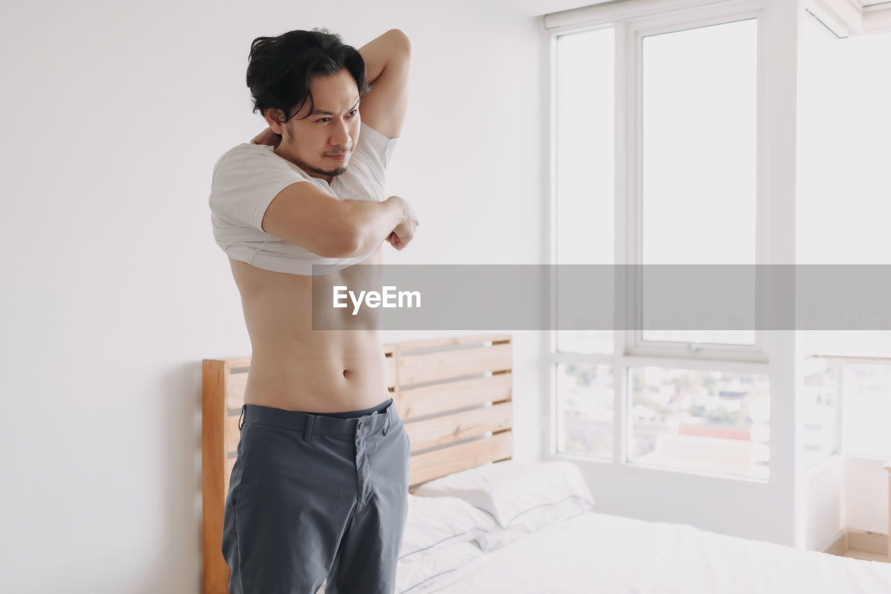 Young man looking away while standing on bed at home