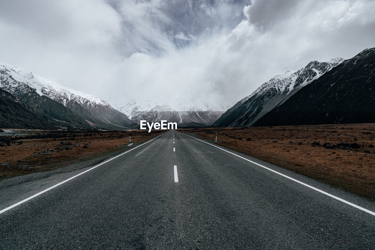 Empty road leading towards mountains against sky