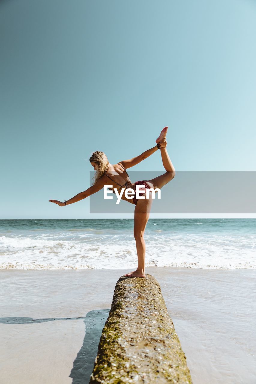 Woman in bikini standing on beach against clear sky