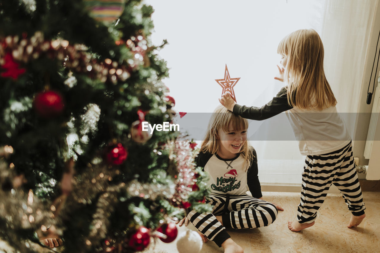 Sisters playing with christmas decoration against wall at home