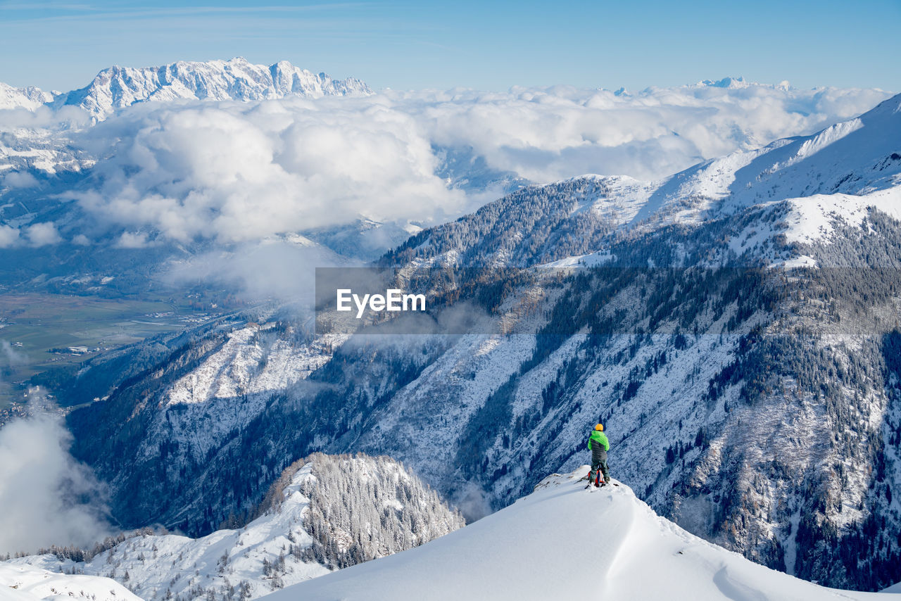 Hiker standing on snowcapped mountain peak while looking at landscape against sky