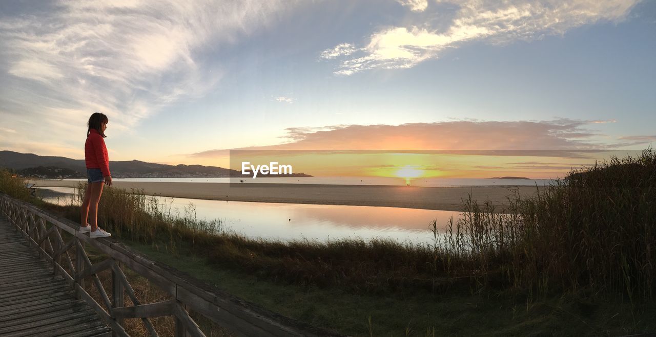 Side view of girl standing on railing against beach during sunset