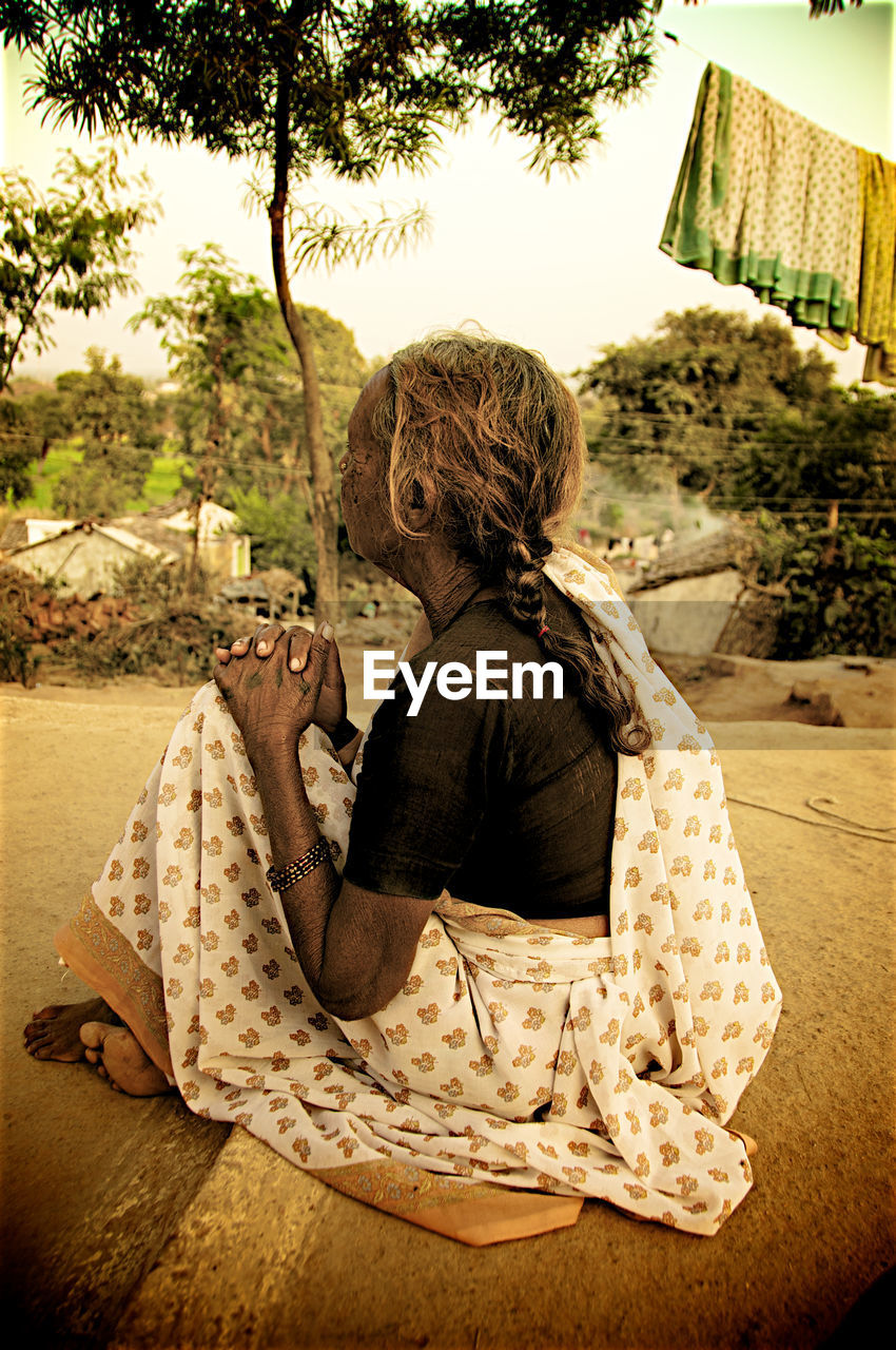 REAR VIEW OF WOMAN SITTING ON TREE LOOKING AT VIEW