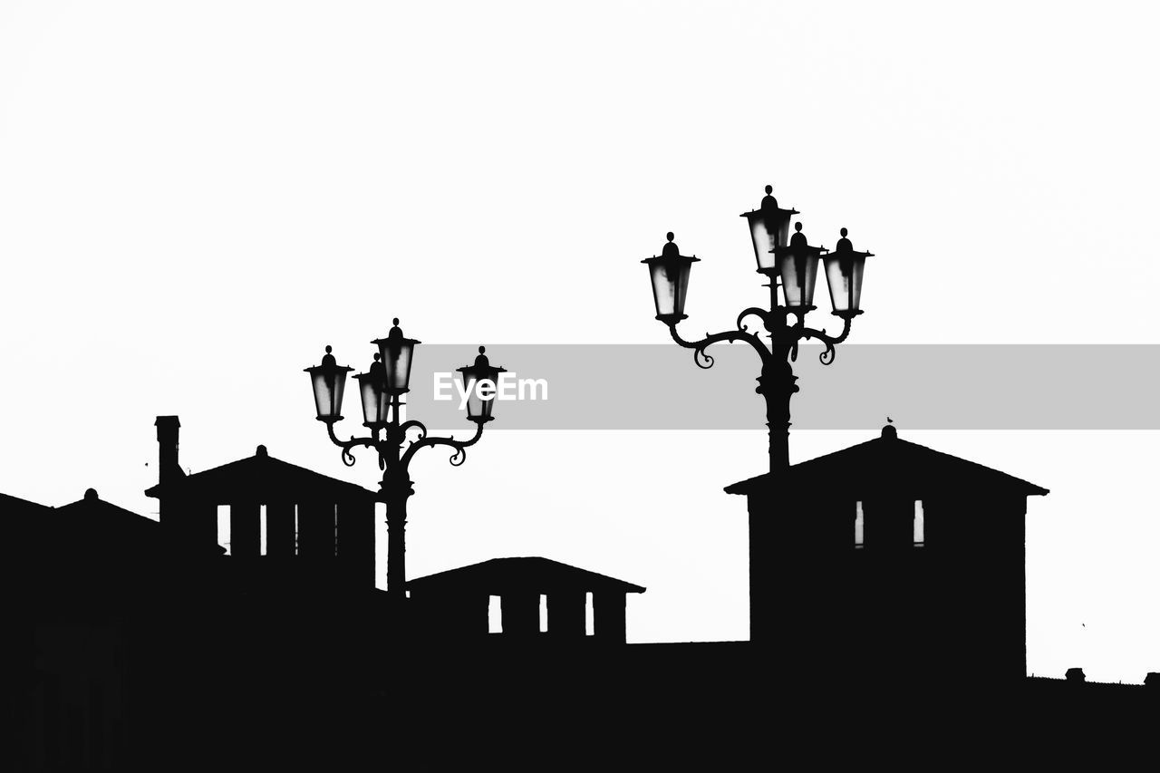 Low angle view of lamps and silhouette building against clear sky