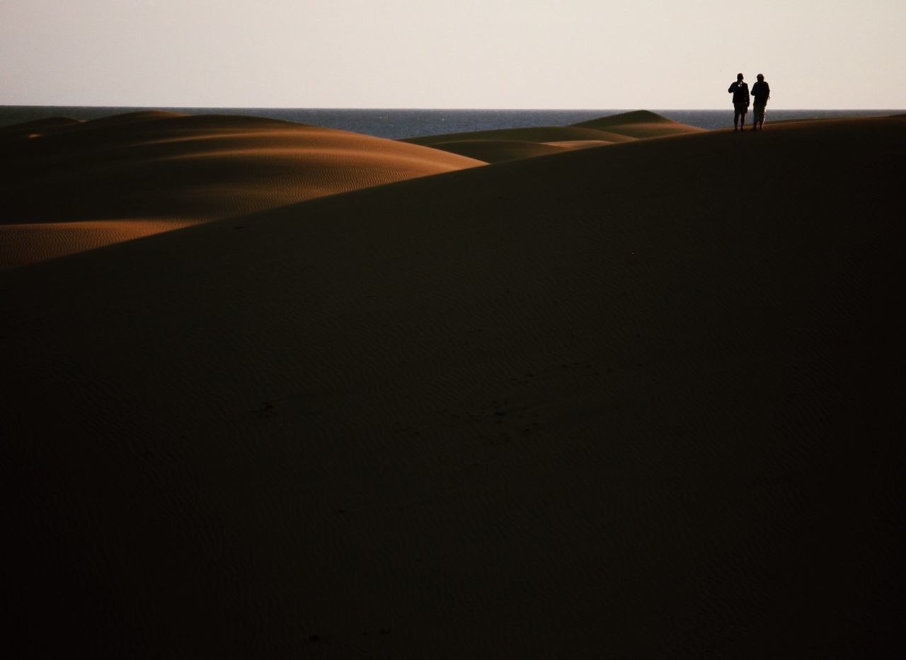 Rear view of two silhouette people standing on sandy beach