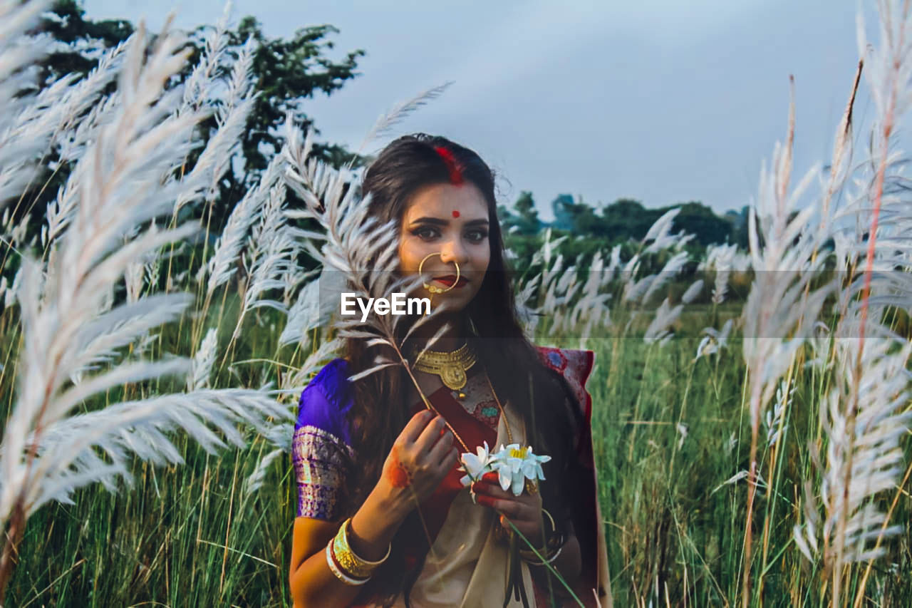 Portrait of young woman wearing sari holding plant on land