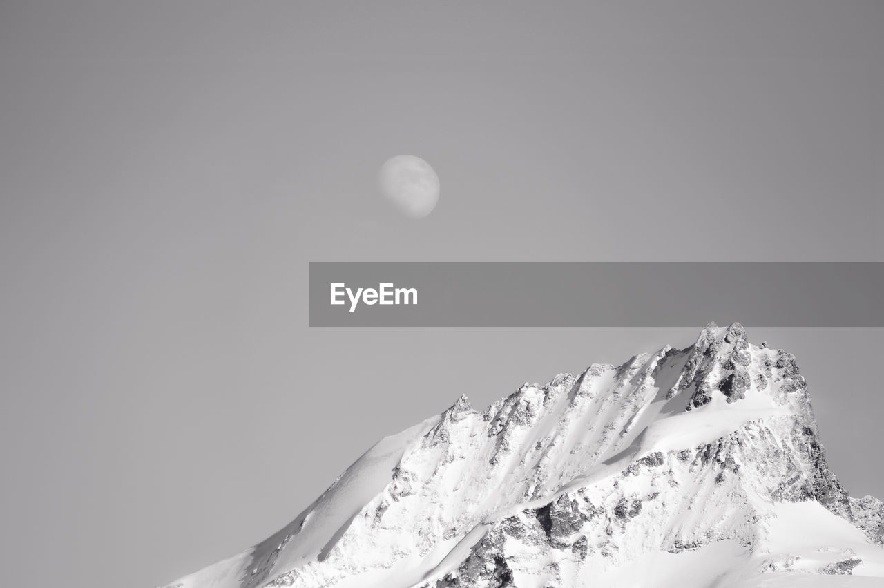 Scenic view of snow covered mountain against moon in clear sky