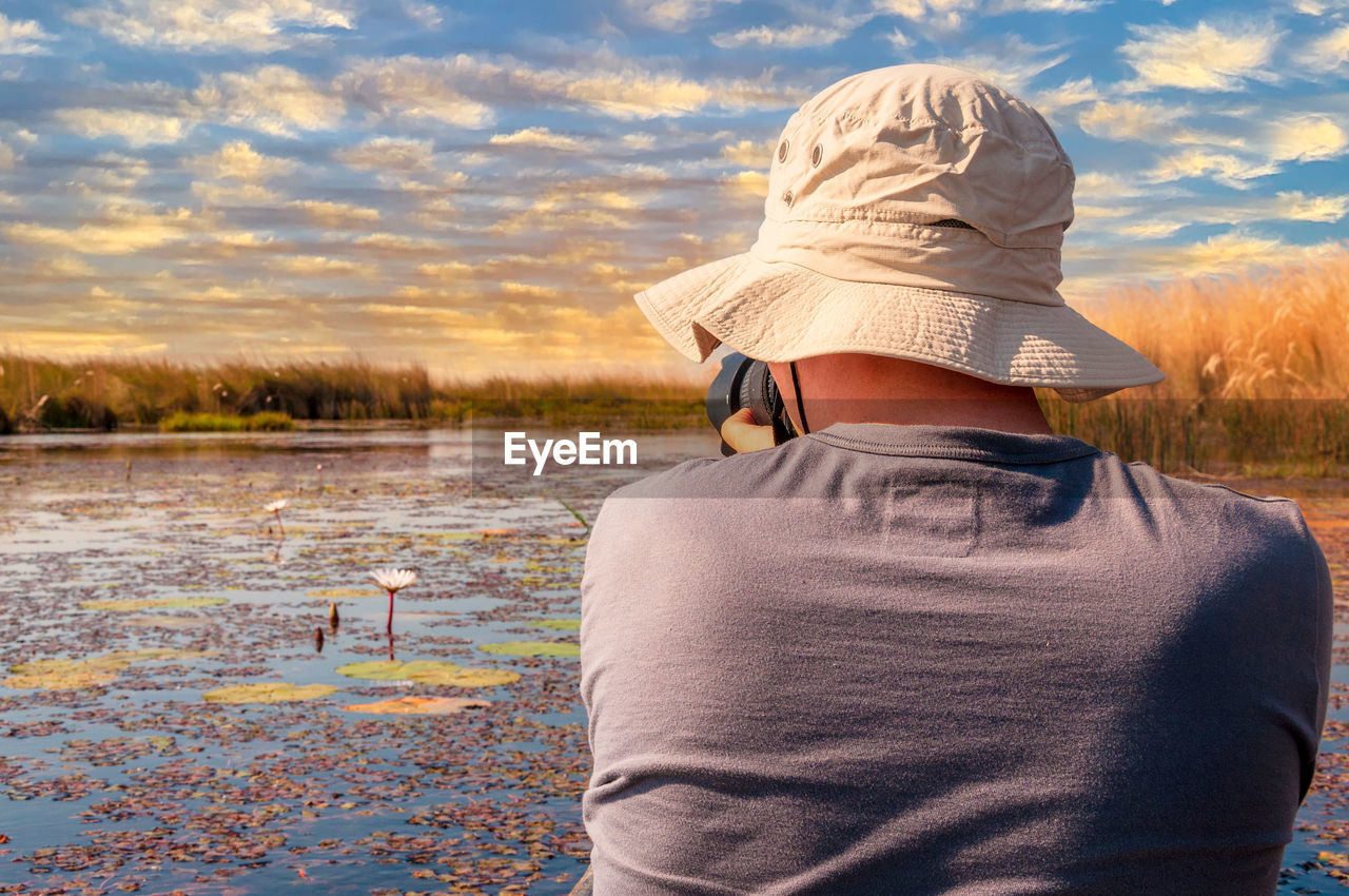 Young photographer man with a hat rides a traditional mokoro on the okavango delta and takes picture