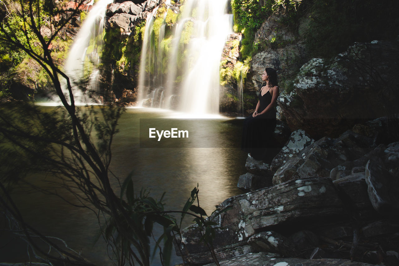 Woman standing on rock by waterfall in forest