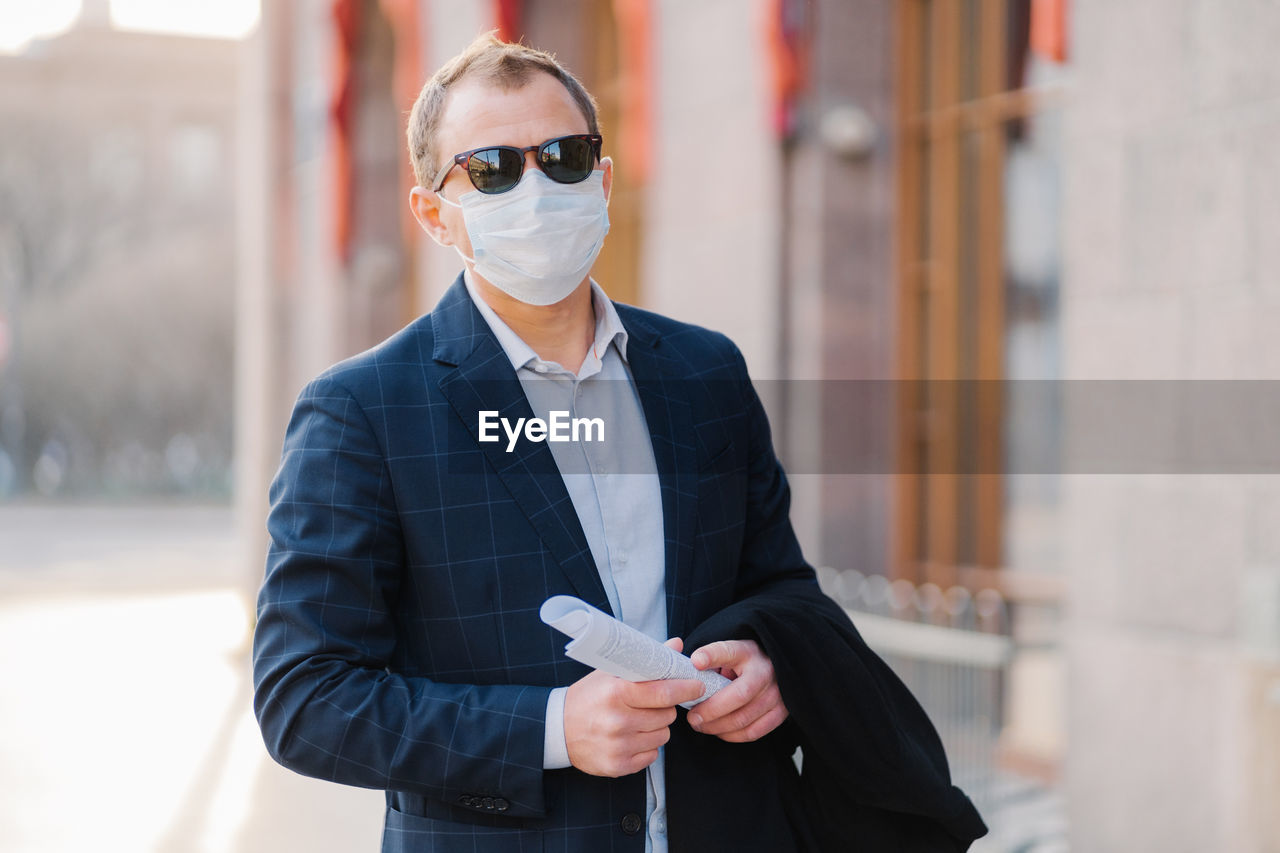 Portrait of businessman wearing mask and sunglasses while standing outdoors