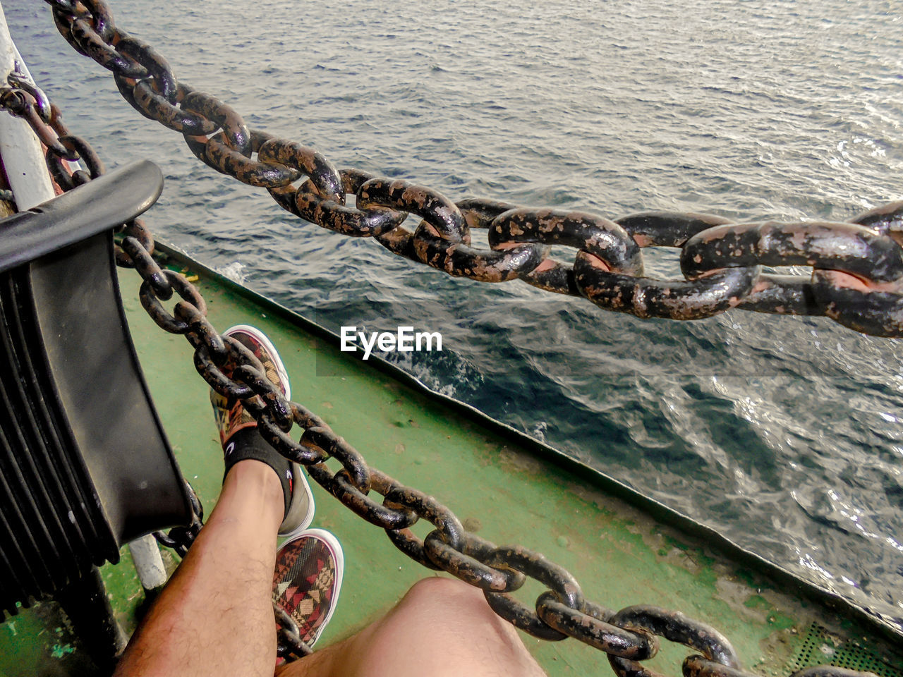 Low section of man sitting by chains on boat in sea