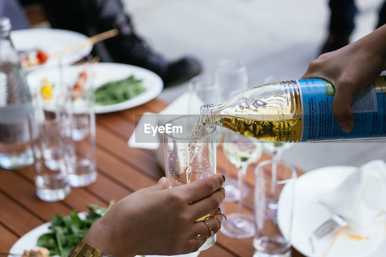 Cropped hand pouring drink to woman at dining table