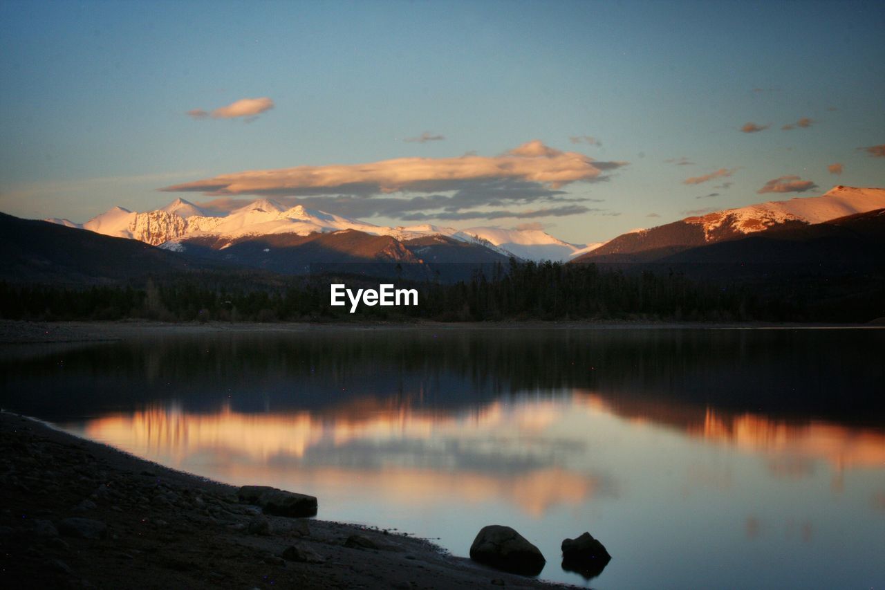 Scenic view of lake and snowcapped mountains at dusk