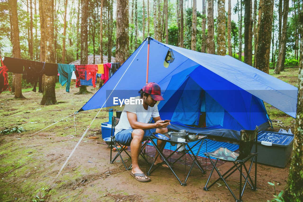Man sitting by tent in forest